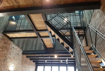 Innenbeleuchtung eines Foyers mit Treppenaufgang, warmen Wandleuchten und Deckenspots an Holz- und Backsteinflächen.