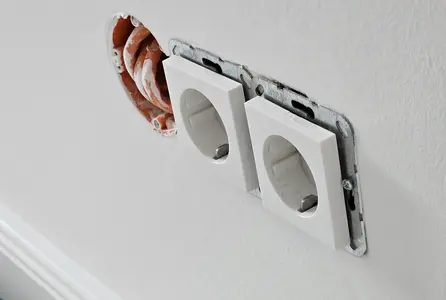 Elektroinstallation einer Doppelsteckdose mit offener Unterputzdose und sichtbaren Leitungen in einer Innenwand.