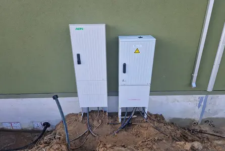 Elektroinstallation im Rohbau mit zwei Anschlusskästen, Kabelzuführungen und Erdarbeiten an einer Gebäudefassade.