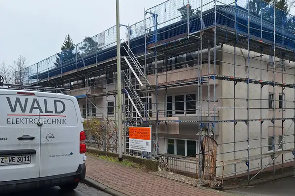 WALD Elektrotechnik Firmenfahrzeug vor einer eingerüsteten Baustelle für Elektroinstallation und Gebäudetechnik.