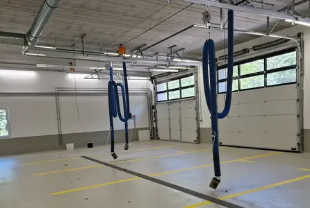 Elektroinstallation in einer Kfz-Halle mit Sektionaltoren, Deckenleitungen und hängenden Absaugschläuchen für Arbeitsplätze.
